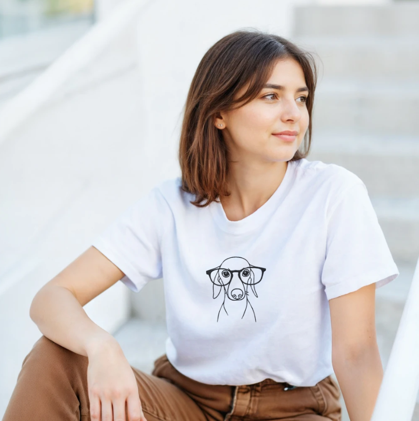 Woman wearing a white personalized dog line art t-shirt outdoors, featuring a minimalist custom pet illustration on the front.